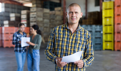 Confident male manager with documents inside a large warehouse