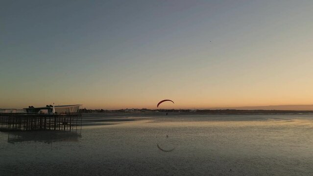 Southport, Lancashire, UK, December 8, 2022; Low aspect aerial clip of the stunning sunset, Southport pier and a low flying paramotor pilot, England, UK