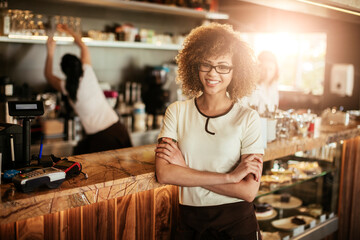 Portrait of a young female barista looking at the camera with crossed arms in a cafe