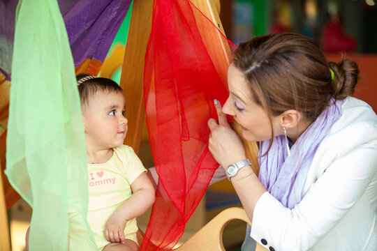 Beautiful ten months baby girl playing with colorful fabrics and her mom. Early stimulation for toddlers concept.