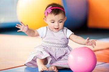 Beautiful ten months baby girl playing with a colorful ball. Early stimulation for toddlers concept.