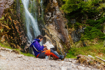 Fototapeta premium white man hiker playing with his dog in a break during a mountain path near a waterfall. travel with pet sport and adventure