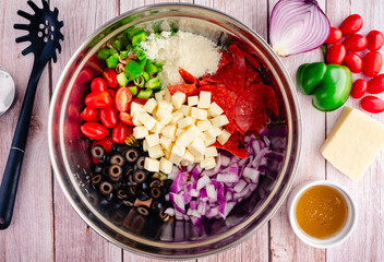 Tricolor Pasta Salad Toppings Before Being Mixed: Chopped and sliced vegetables and cheeses on top of pasta in a large mixing bowl