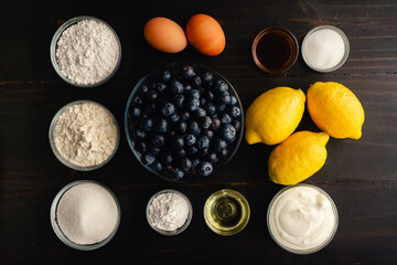 Blueberry Muffins with Lemon Glaze on a Dark Wood Background: Fresh blueberries, lemons, and other raw ingredients on a rustic wooden background
\
