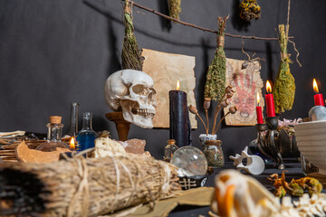 Occult and esoteric witchcraft still life. Halloween background with magic objects. Black candles, skull, crystal stones, and potions vials for witch. Mystic witchery background with dry weeds.