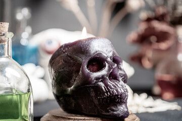 Human skull candle selective focus, arranged with black candles and spell potion vials on...