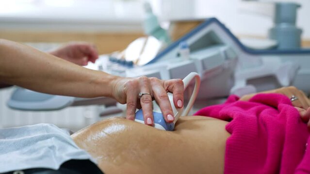 Female doctor's hand moving the ultrasound device by the patient's belly. Ultrasonic pregnancy scanning.