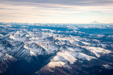 View of the snow covered Andes mountains and volcanoes through the window of an airplane at sunrise