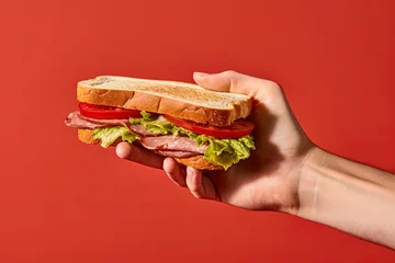 Poster Hand holding tasty sandwich on a red background © agungai
