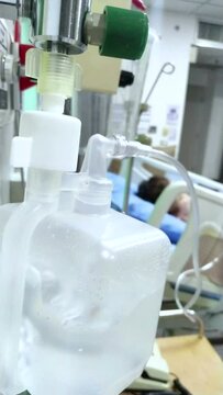 Oxygen humidifier for nasal cannula, patient on hospital bed on blurred background. vertical.