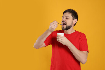 Handsome man eating tasty yogurt on orange background