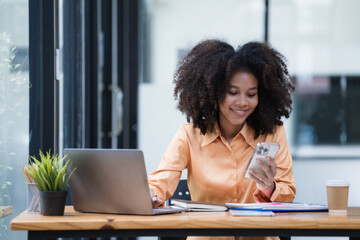 Portrait of a beautiful confident businesswoman using a laptop computer holding a mobile phone...
