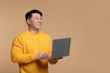 Happy man with laptop on beige background, space for text