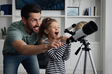 Little girl with his father looking at stars through telescope in room