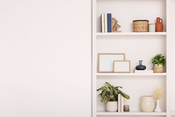 Interior design. Shelves with stylish accessories, potted plants and frames near white wall. Space...
