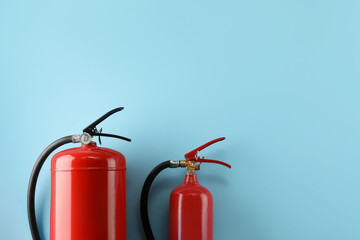 Different fire extinguishers on light blue background, flat lay. Space for text - obrazy, fototapety, plakaty