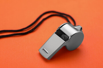 One metal whistle with black cord on orange background, closeup
