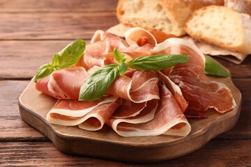 Slices of tasty jamon and basil on wooden table, closeup