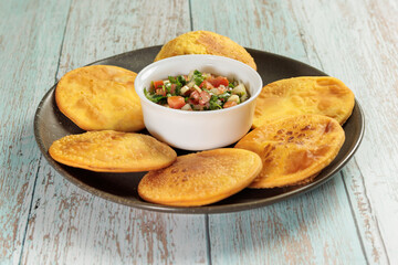 Sopaipillas of pumpkin or squash in round plate on wooden table and bowl with pebre in the center. typical chilean food concept
