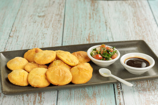 Sopaipillas, pumpkin or squash in rectangular plate on wooden table, bowl with pebre and chancaca, copy space. Typical Chilean food concept