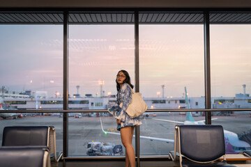 Travel standing with luggage watching sunset at airport window Unknown woman looking at lounge...