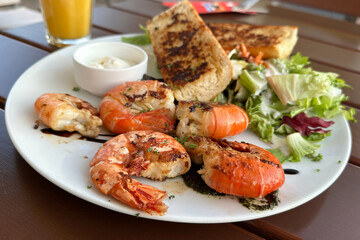 Grilled tiger prawns served with garlic breads and salad in white plate