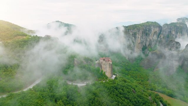 Aerial view of a valey Meteora with clifs covered by mist.  Epic view of Holy Monastery of Rousanos - Saint Barbara complex on the top of meteora cliff among clouds and mist. A UNESCO Site. 