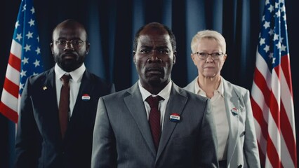 Medium portrait shot of middle-aged African American presidential candidate, black male vice president, and Caucasian female press secretary, posing during election campaign in front of USA flag