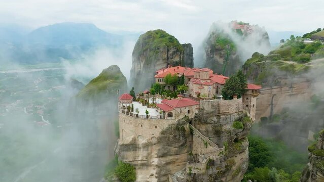 Varlaam Meteora Monastery in Greece, rising out of the mist. Amazing mystical panoramic landscape. Epic view of monastery complex on the top of meteora cliffs among clouds and mist. A UNESCO World Her