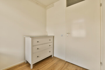 an empty room with white walls and wooden floors, there is a chest of drawers on the right hand side
