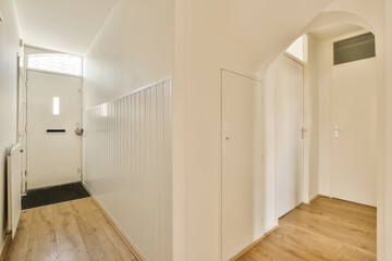 an empty hallway with white walls and wood flooring on the right side, there is a door leading to another room