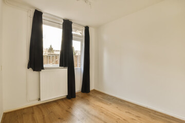 an empty room with wooden floors and white walls, black drapes hanging from the window to the right side