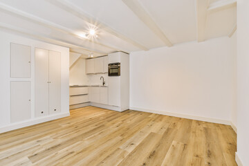 an empty living room with wood flooring and white cupboards on the wall to the right is a microwave