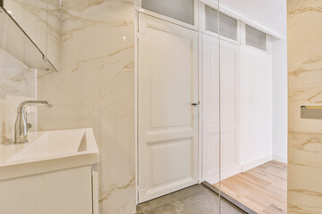 a modern bathroom with marble walls and flooring, including a white wash basin bowl on the right handwasher