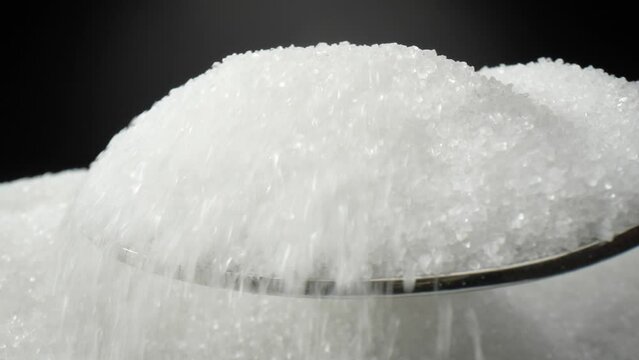 In a macro video, a silver spoon delicately scoops up fine white sugar crystals. Each sparkling grain glistens as it gracefully clings to the spoon's concave surface. Sweet concept. Sugar background
