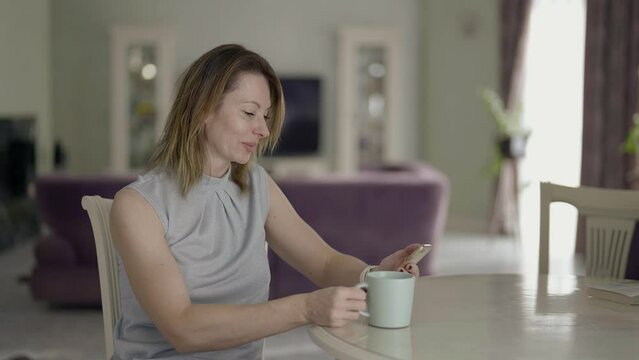 attractive middle-aged European woman uses a smartphone in the morning at home in the kitchen