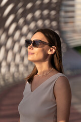 Summer portrait of a young brunette woman in a beige outfit and sunglasses. Urban abstract background, beautiful refraction of natural light.