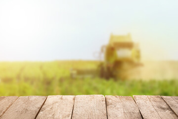 Fototapeta premium Empty wooden table in green field with combine harvester