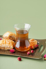 Glass cup of tea with Turkish delight and dry roses on color background