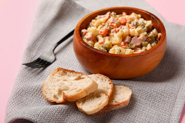 Bowl of tasty Olivier salad and bread on pink background