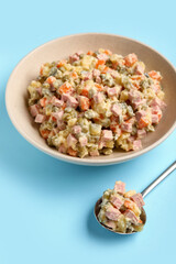 Bowl of tasty Olivier salad on blue background