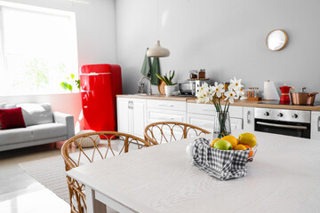 Basket with fruits and narcissus flowers on table in light kitchen
