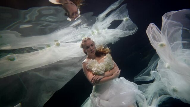 mysterious woman underwater, dream and fantasy, bewitched bride in wedding dress floating in water