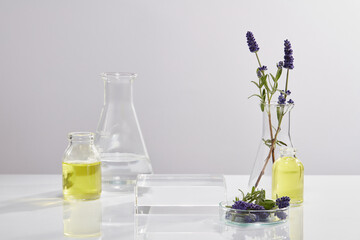 Transparent podium in square-shaped decorated with laboratory glassware over white background. Pedestal or platform for beauty products presentation of Lavender (Lavandula) extract