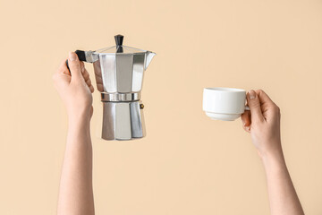 Female hands holding cup and geyser coffee maker on beige background