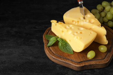 Board with tasty Swiss cheese on black background