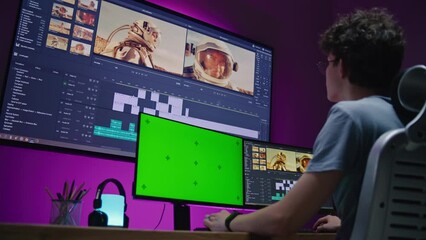 Young video maker edits movie about space mission, works at home office. Film footage and software interface with tools and sound tracks on big digital screen. Computer monitor with green screen.