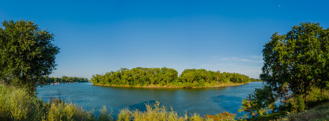 Panorama of curve in sacramento river framed by two oak trees growing on the levee 