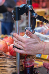 Squeeze juice from fresh pomegranates using a manual press at a street food market