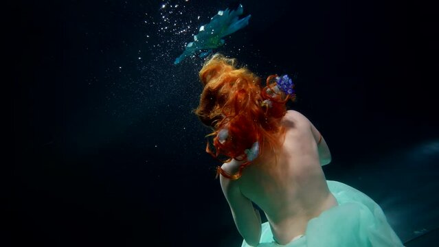 enigmatic female figure in dark deepness of magic ocean, mermaid from fairytale, back view